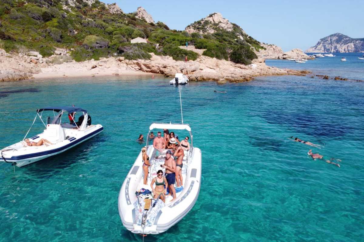 Gita in barca verso Tavolara, vista dei passeggeri che osservano l'isola dal mare, sole alto e acqua trasparente