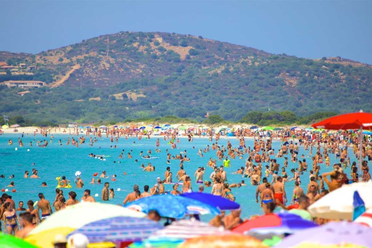 Panoramica dall'alto della spiaggia La Cinta di San Teodoro con famiglie, bambini che giocano e acqua turchese. Atmosfera estiva e rilassata.